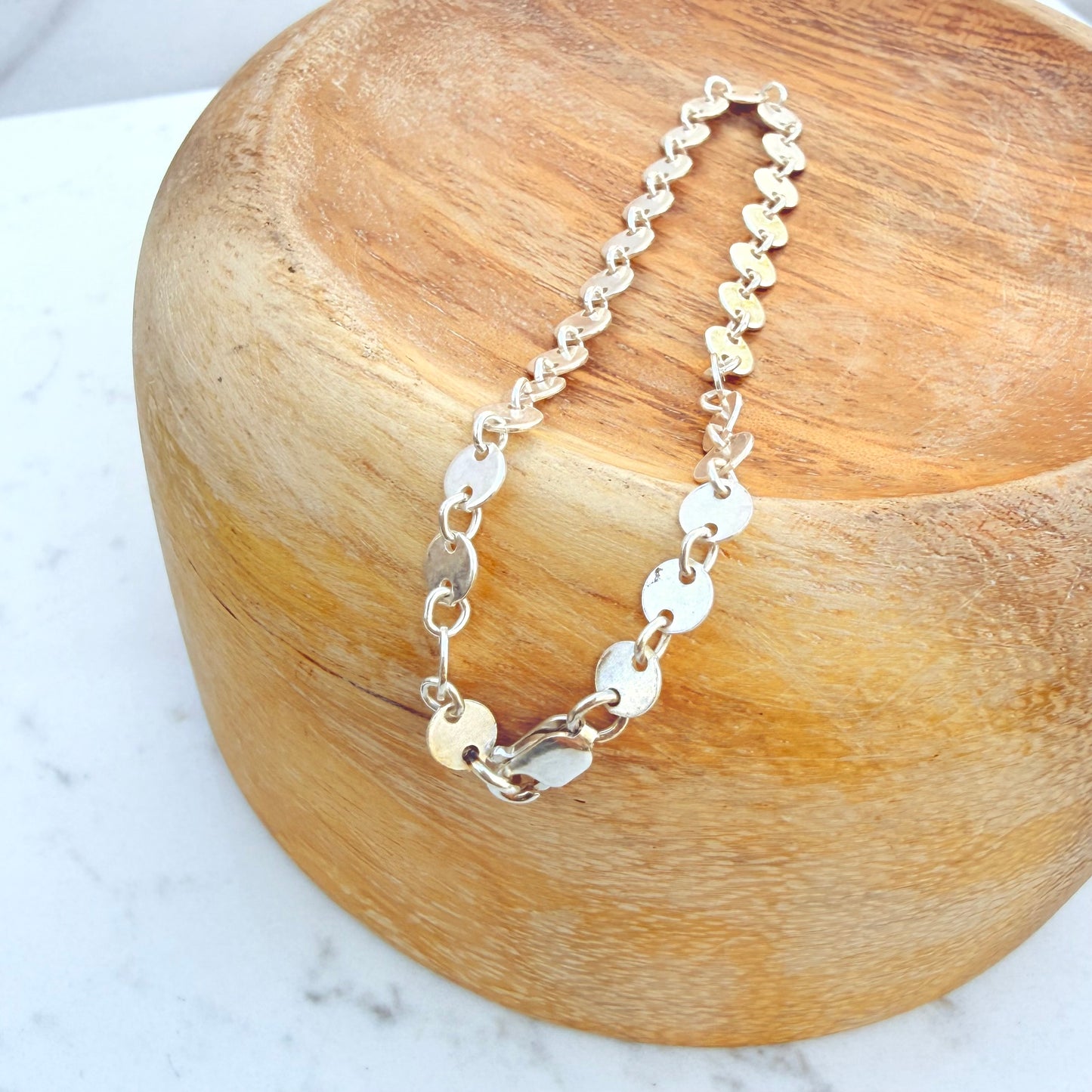 Silver sequin chain bracelet on a wooden block with a marble background