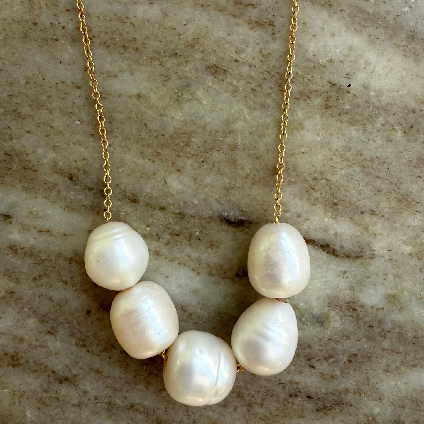 Pearl necklace with gold chain on a textured stone surface