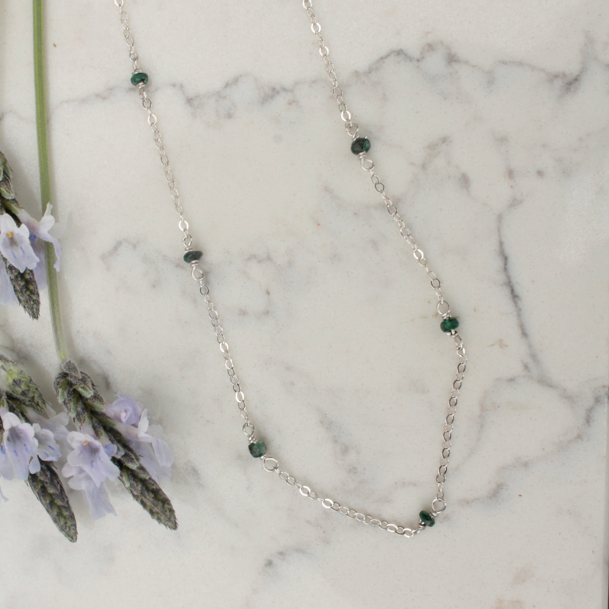 Emerald beads strung on sterling silver chain necklace on white marble background