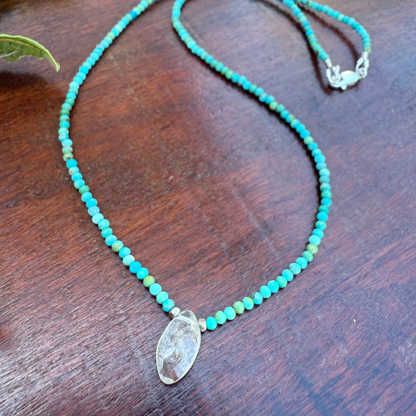 Turquoise beaded necklace with a clear stone pendant on a wooden surface