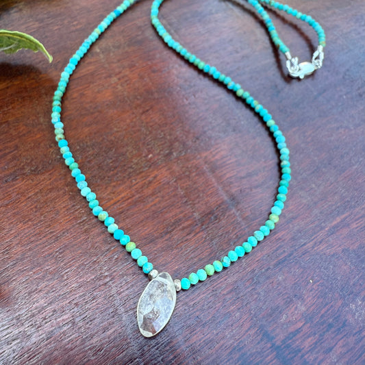 Turquoise beaded necklace with a clear stone pendant on a wooden surface