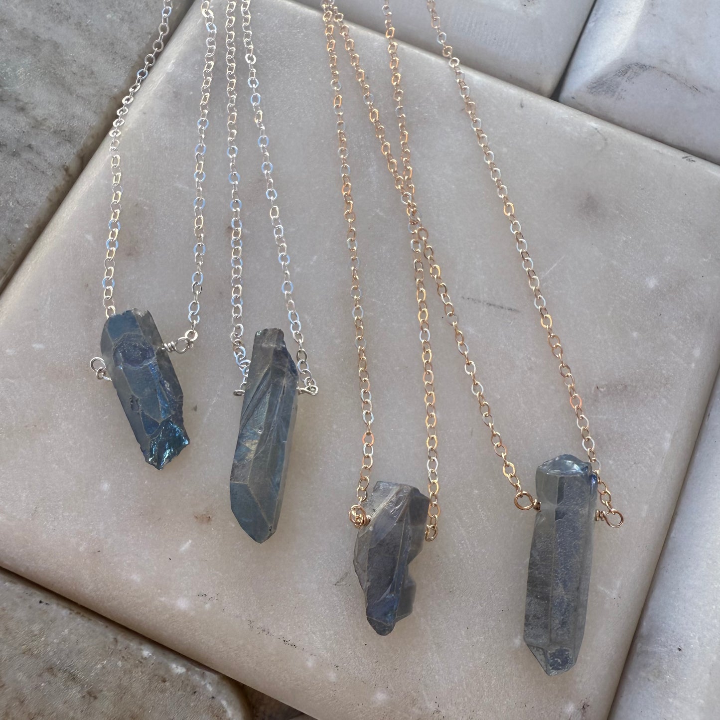 Four necklaces with quartz pendants on a marble surface