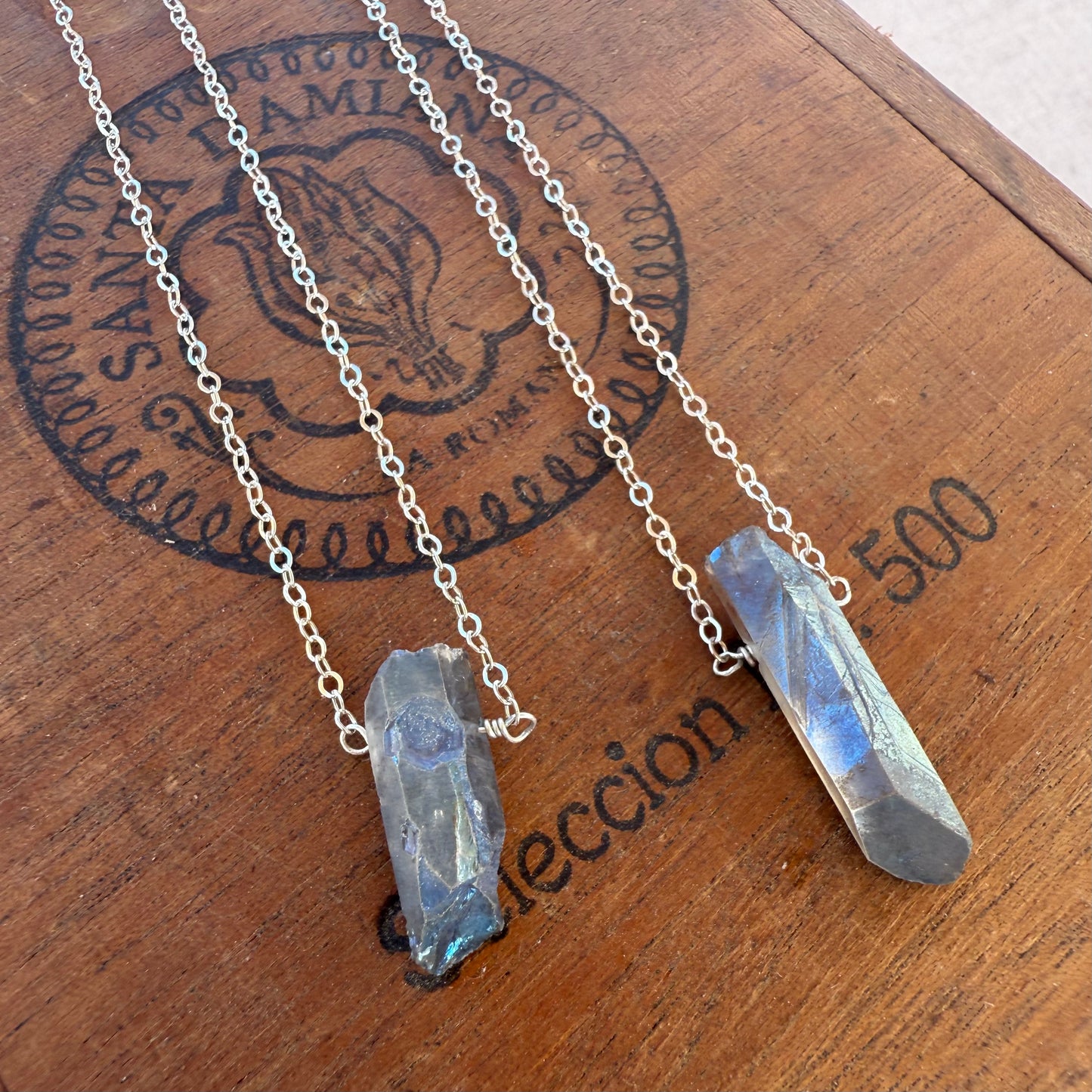 Two crystal necklaces on a wooden surface with a brand logo.