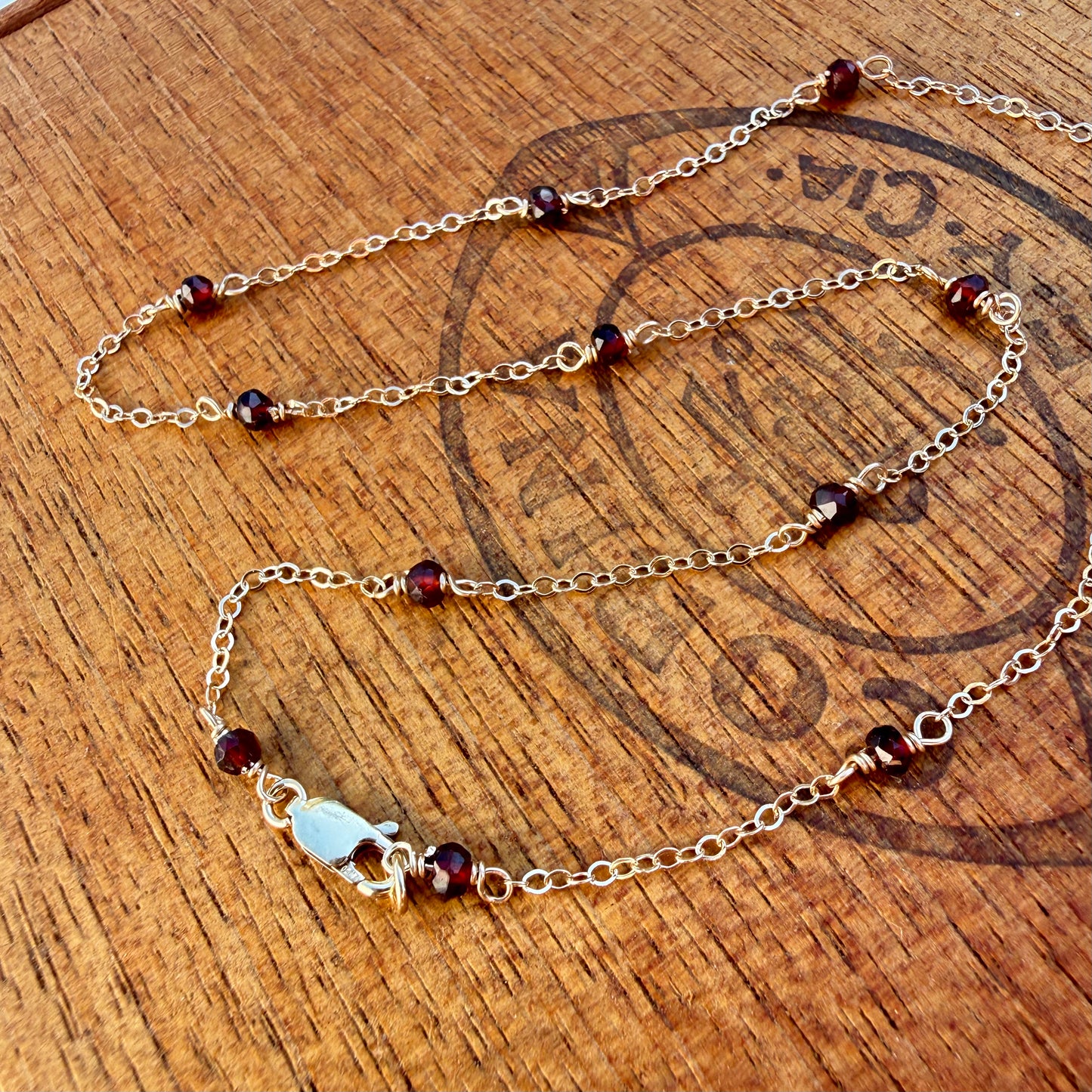 Gold filled chain necklace with red garnet beads on a wooden surface