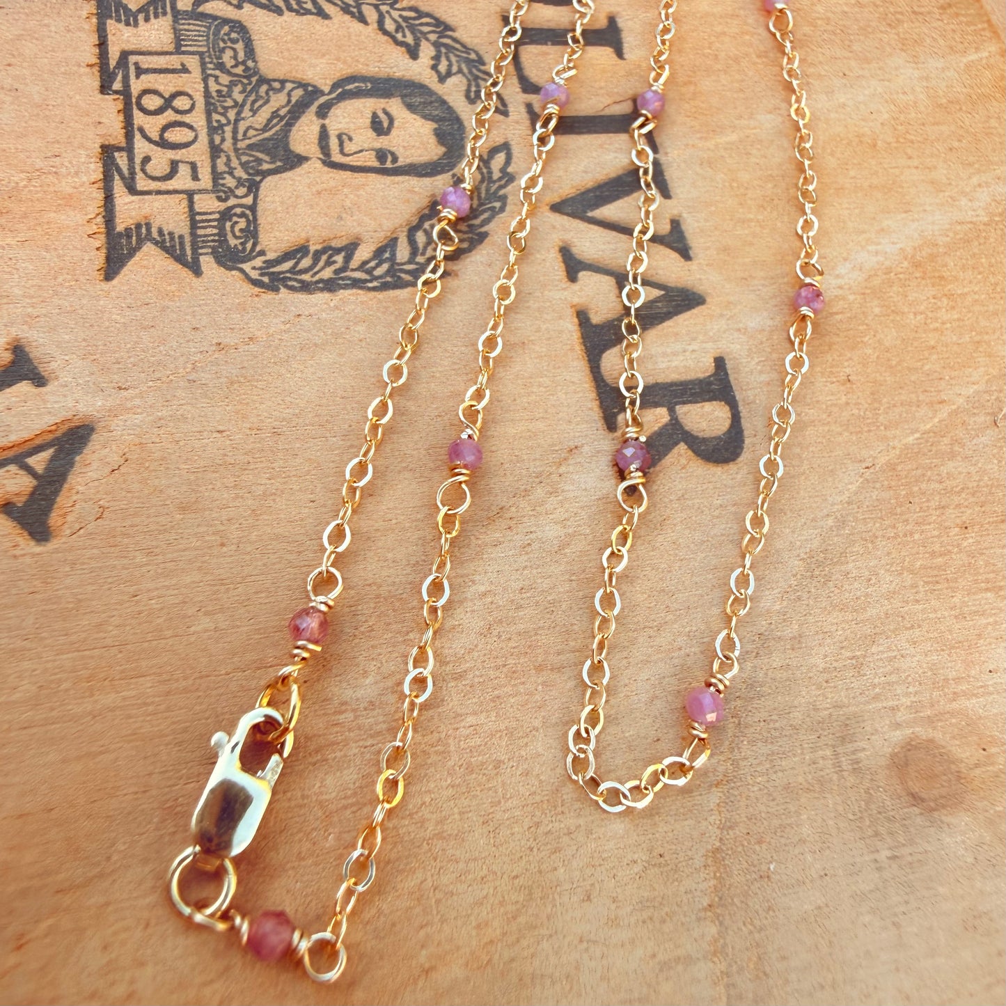 Gold chain necklace with pink tourmaline beads on a rustic wooden background