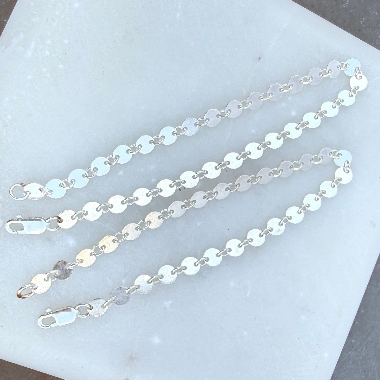 Two silver chain necklaces on a white stone surface