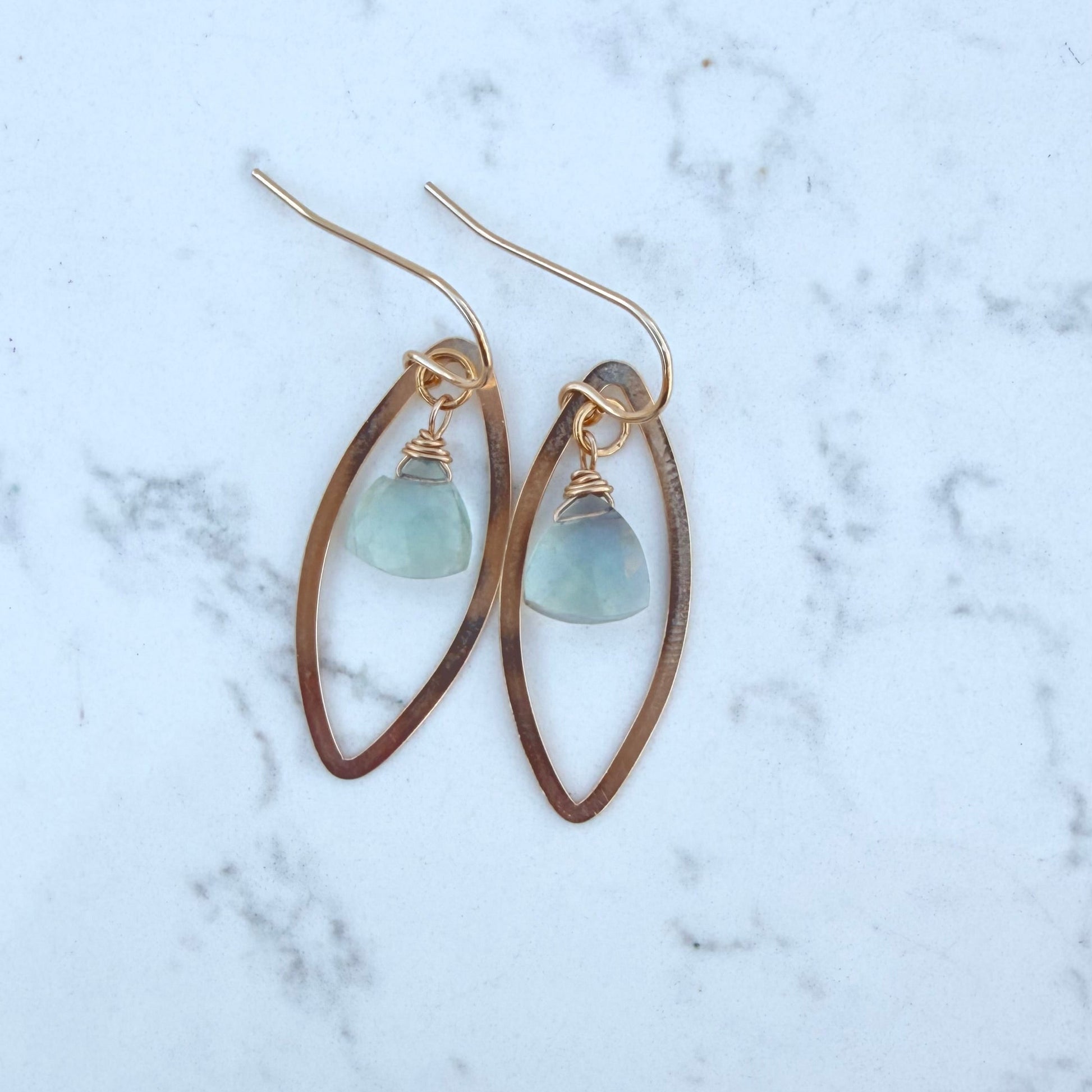 Gold earrings with green fluorite gemstones on a marble surface