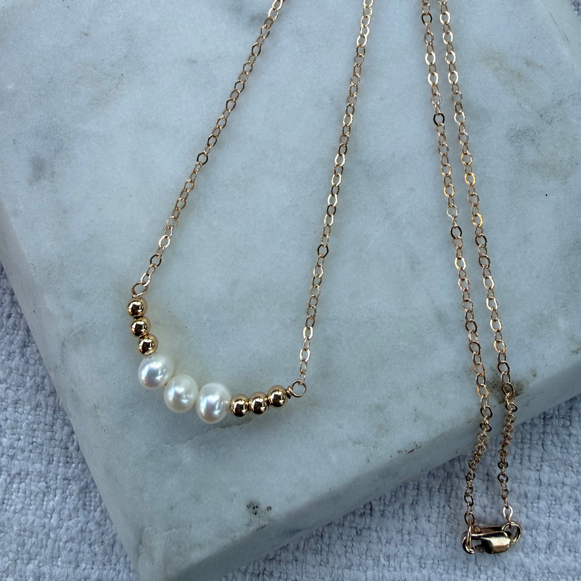 Gold necklace with pearl accents on a marble surface