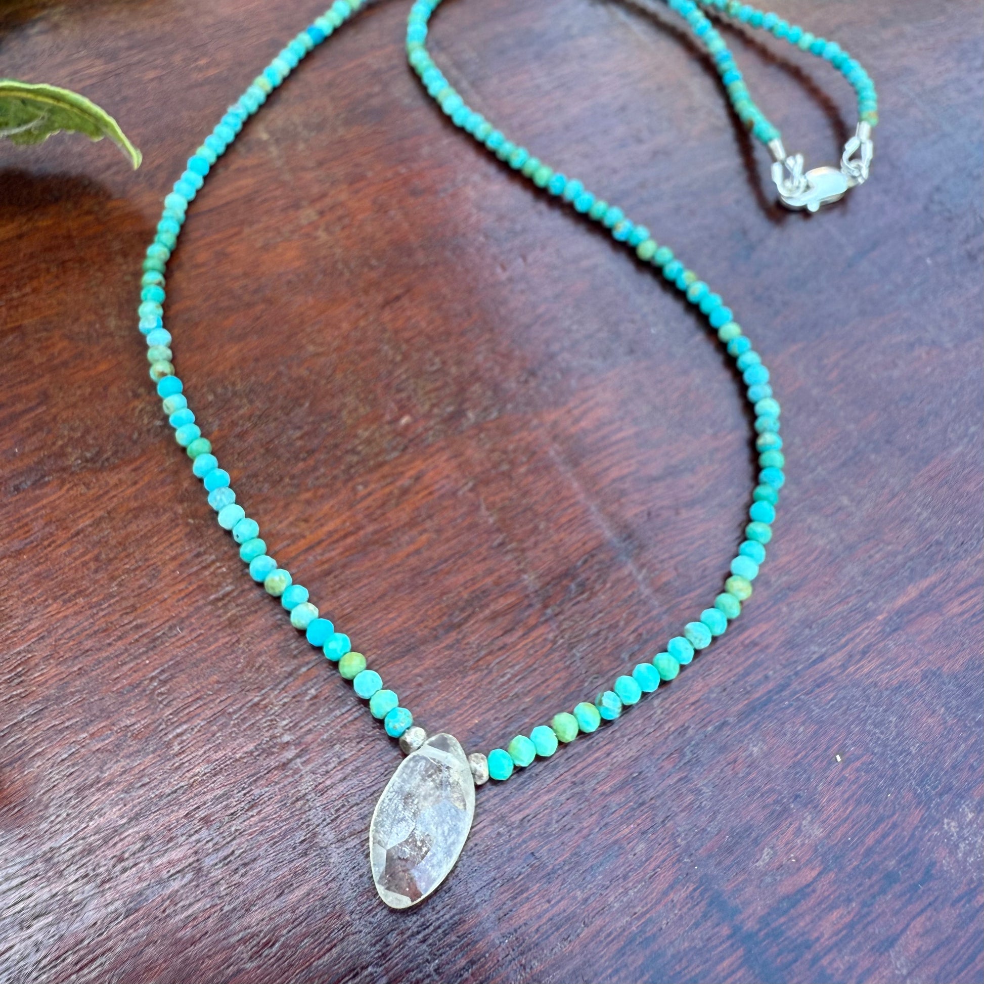Turquoise beaded necklace with a clear stone pendant on a wooden surface