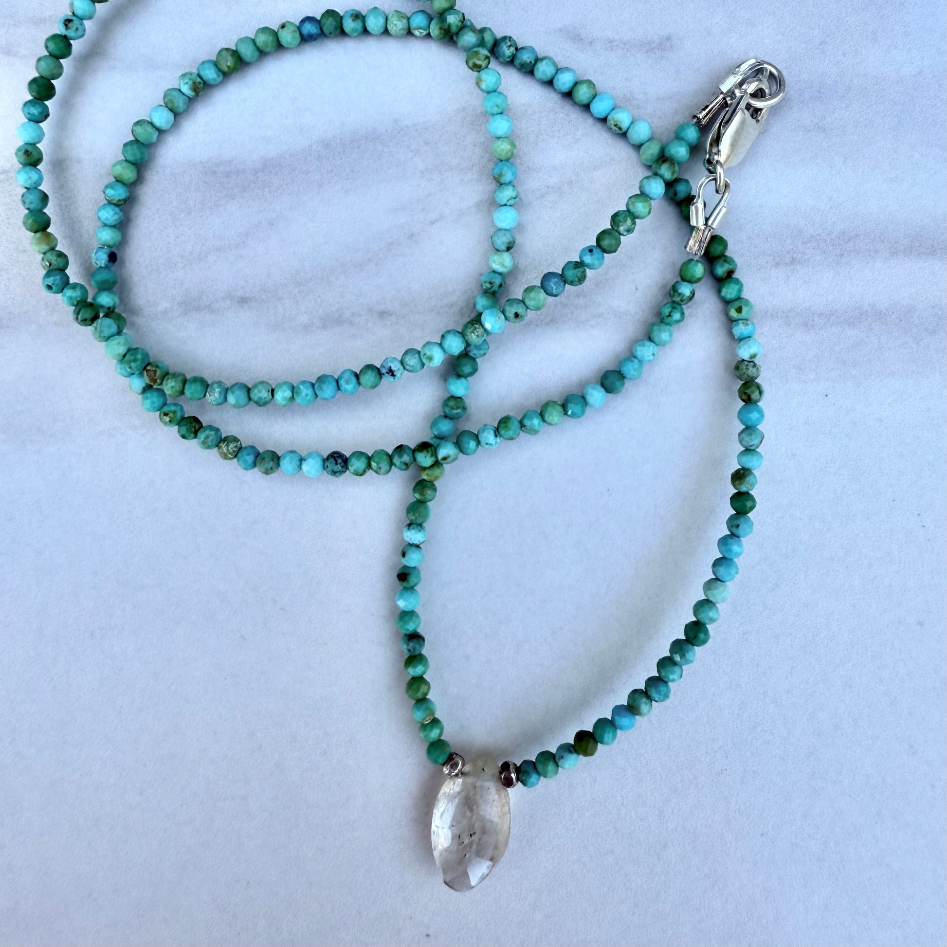 Beaded necklace with a clear rutile quartz pendant on a marble surface