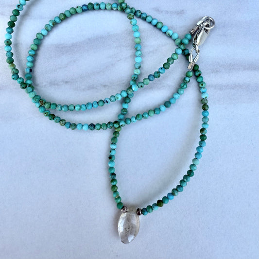 Beaded necklace with a clear rutile quartz pendant on a marble surface