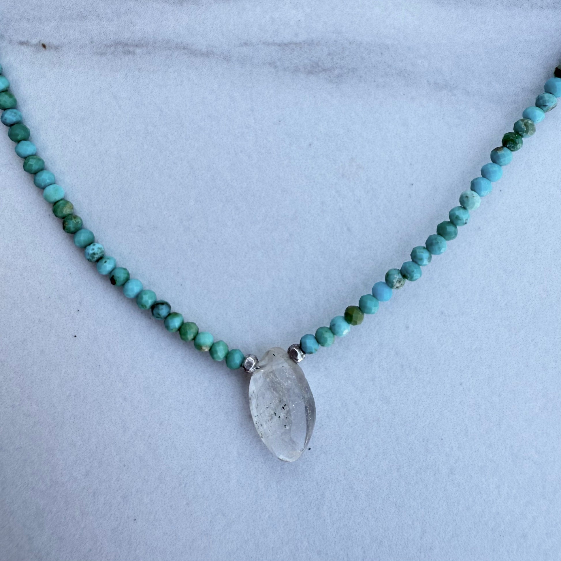 Necklace with turquoise beads and a clear  rutile quartz pendant on a light background