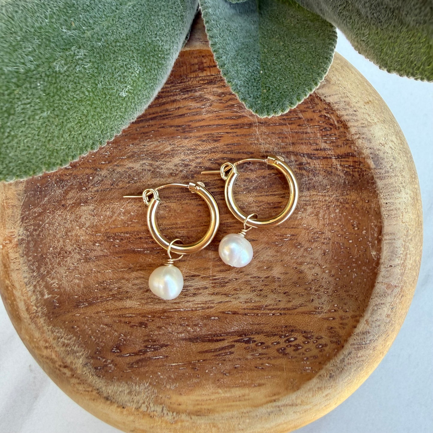 Gold hoop earrings with pearl drops on a wooden surface