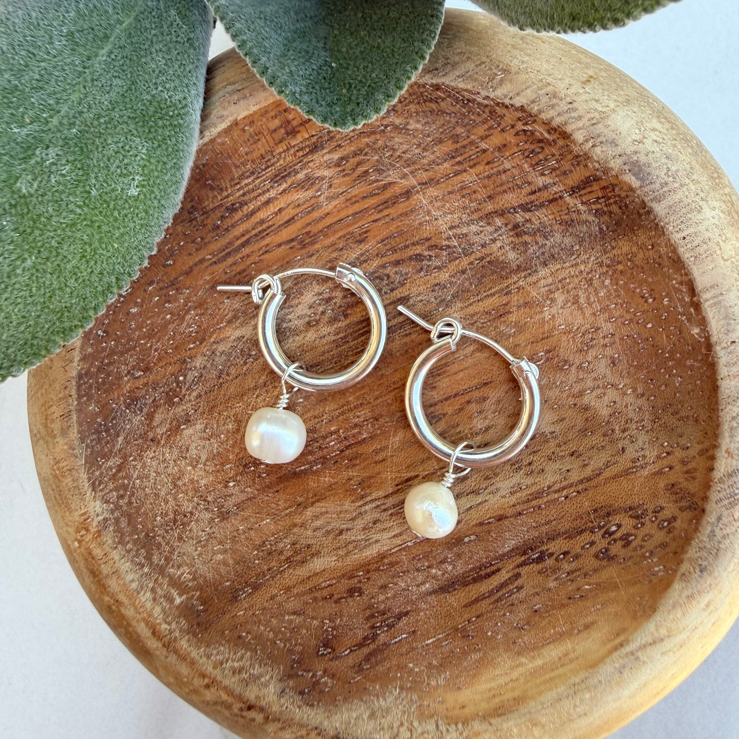 Silver hoop earrings with pearl drops on a wooden surface.