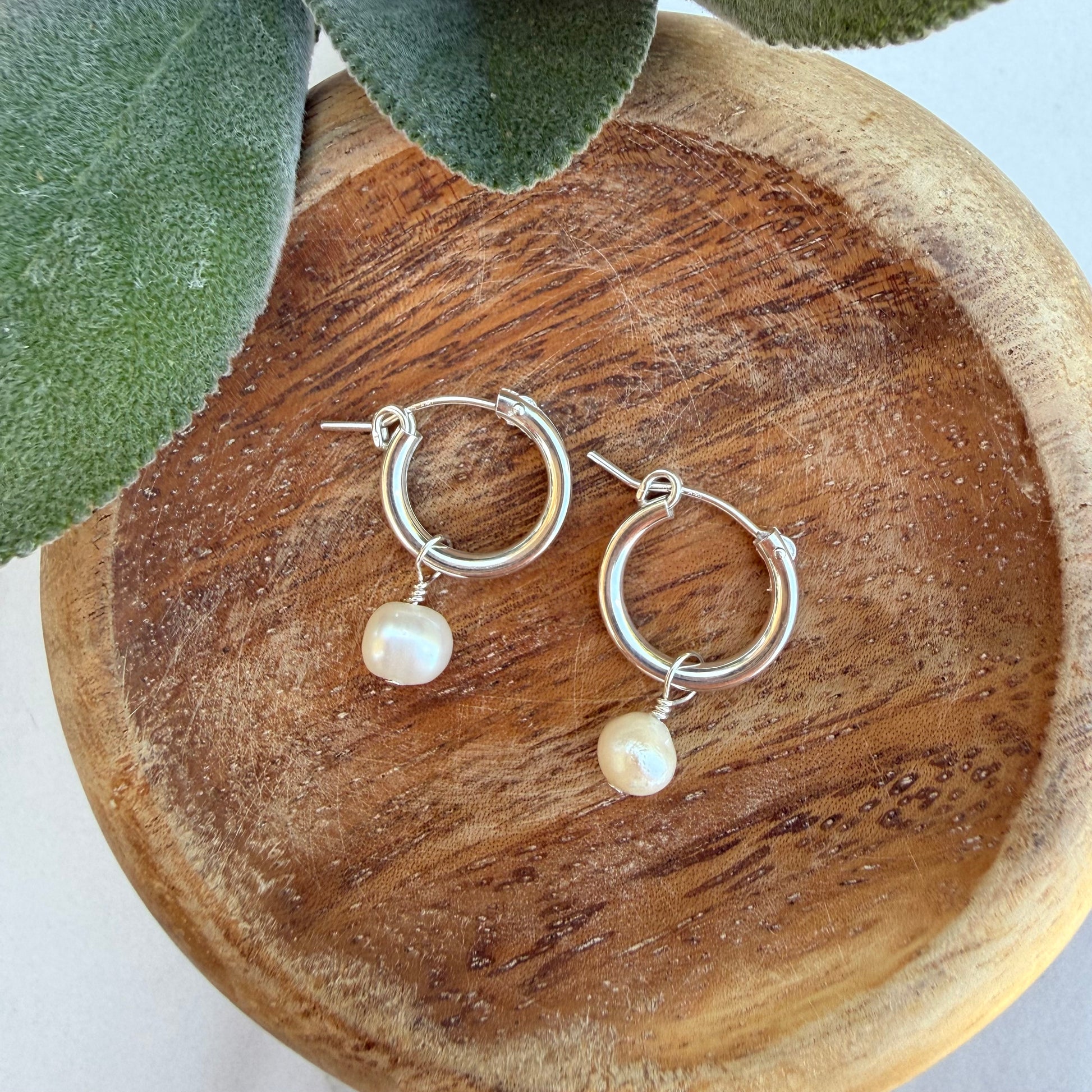Silver hoop earrings with pearl drops on a wooden surface.