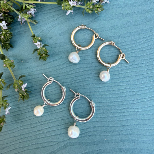 Gold and silver hoop earrings with pearl drops on a textured blue surface with green leaves.